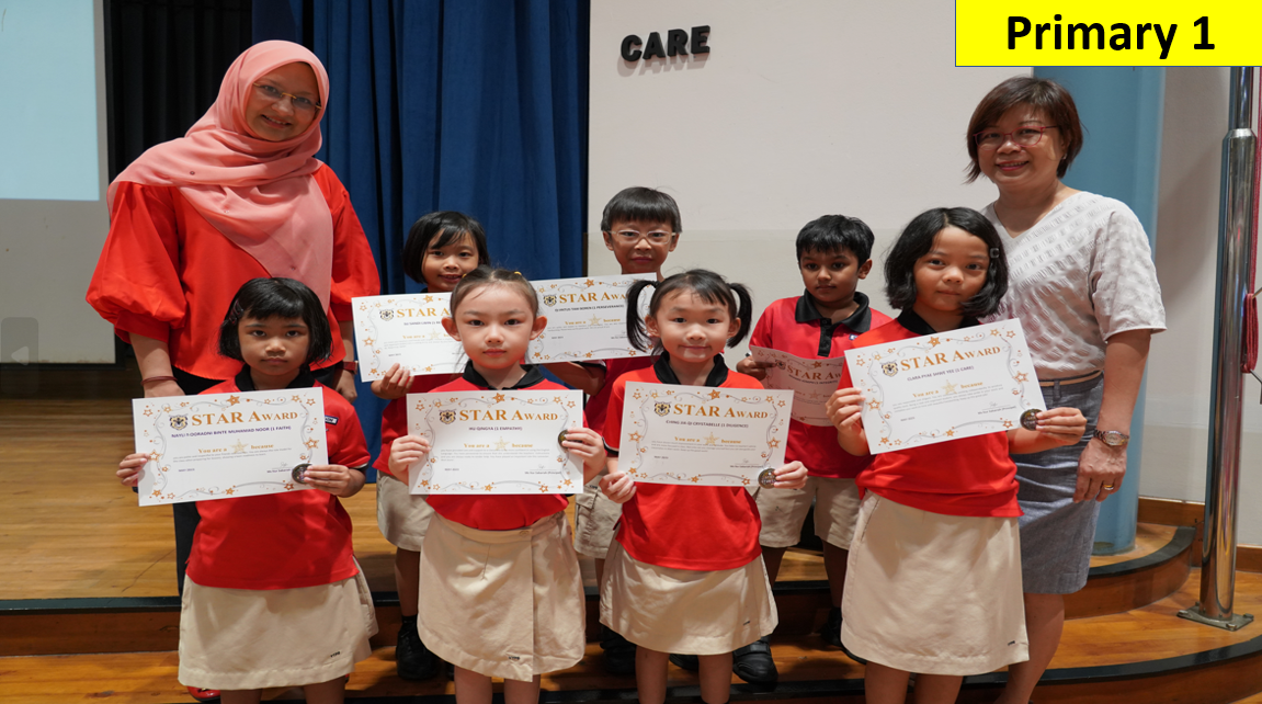 Primary 1 students holding Star Award certificates pose with two teachers on a stage.